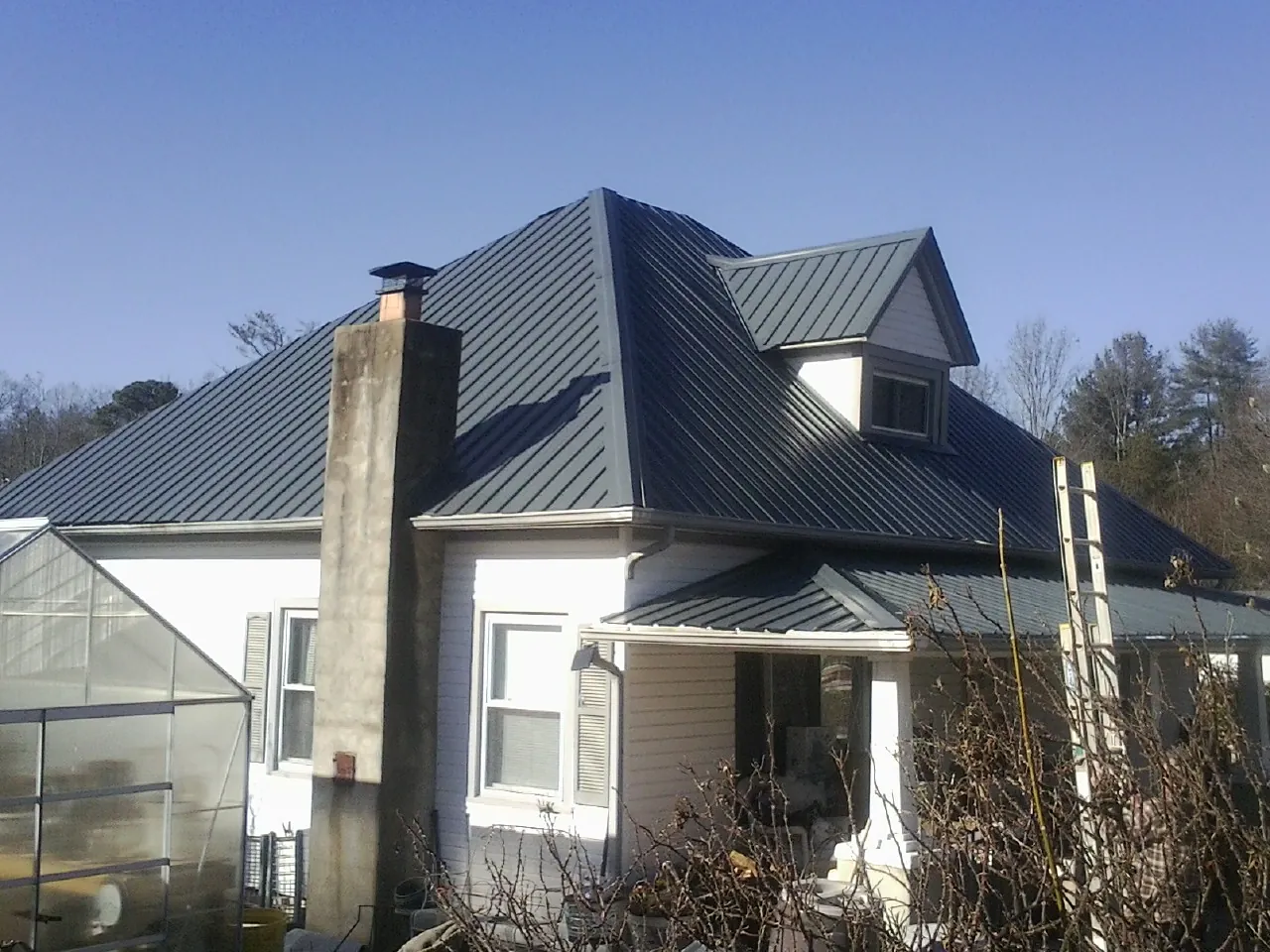 Dark blue standing seam metal roof on a white farmhouse with dormer — Slate & Tile Roof Repair by Roofing Brothers in Middlebury Center