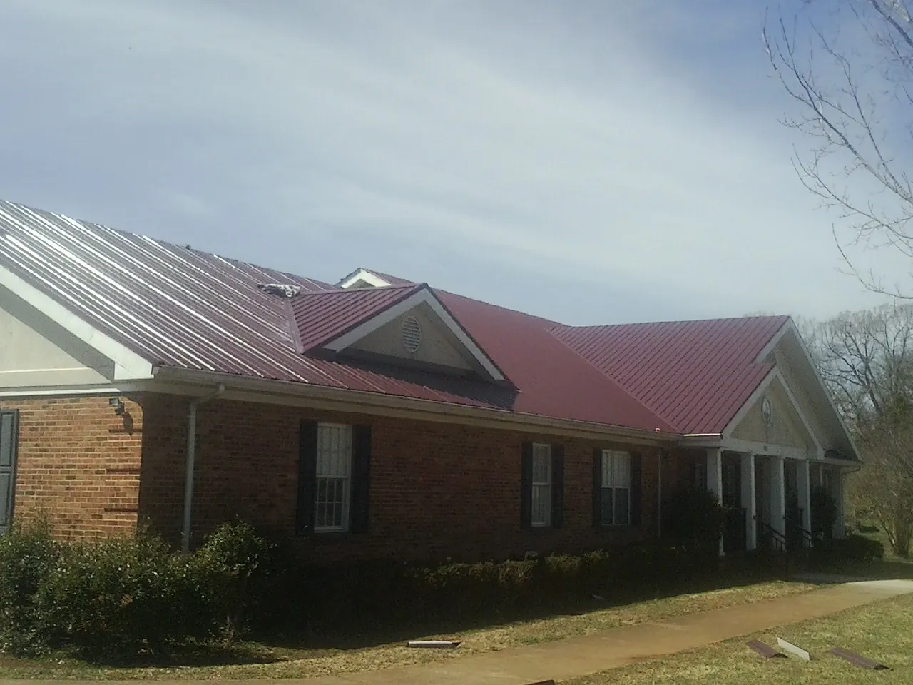Red metal roof with gabled entries on a long brick building, from a Hail Damage Roof Repair job in Middlebury Center