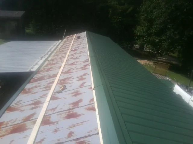 Old rusted panels beside newly installed green metal roofing — Wind Damage Roof Repair by Roofing Brothers in Middlebury Center