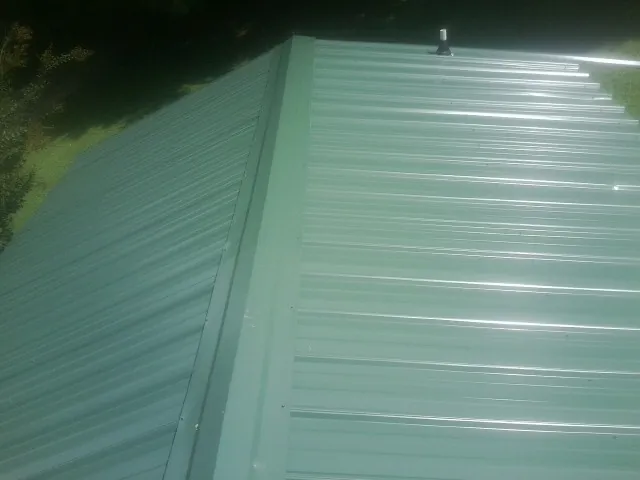 New green metal panels meeting at the ridge of a roof — Flat Roof Repair work by our crew in Middlebury Center