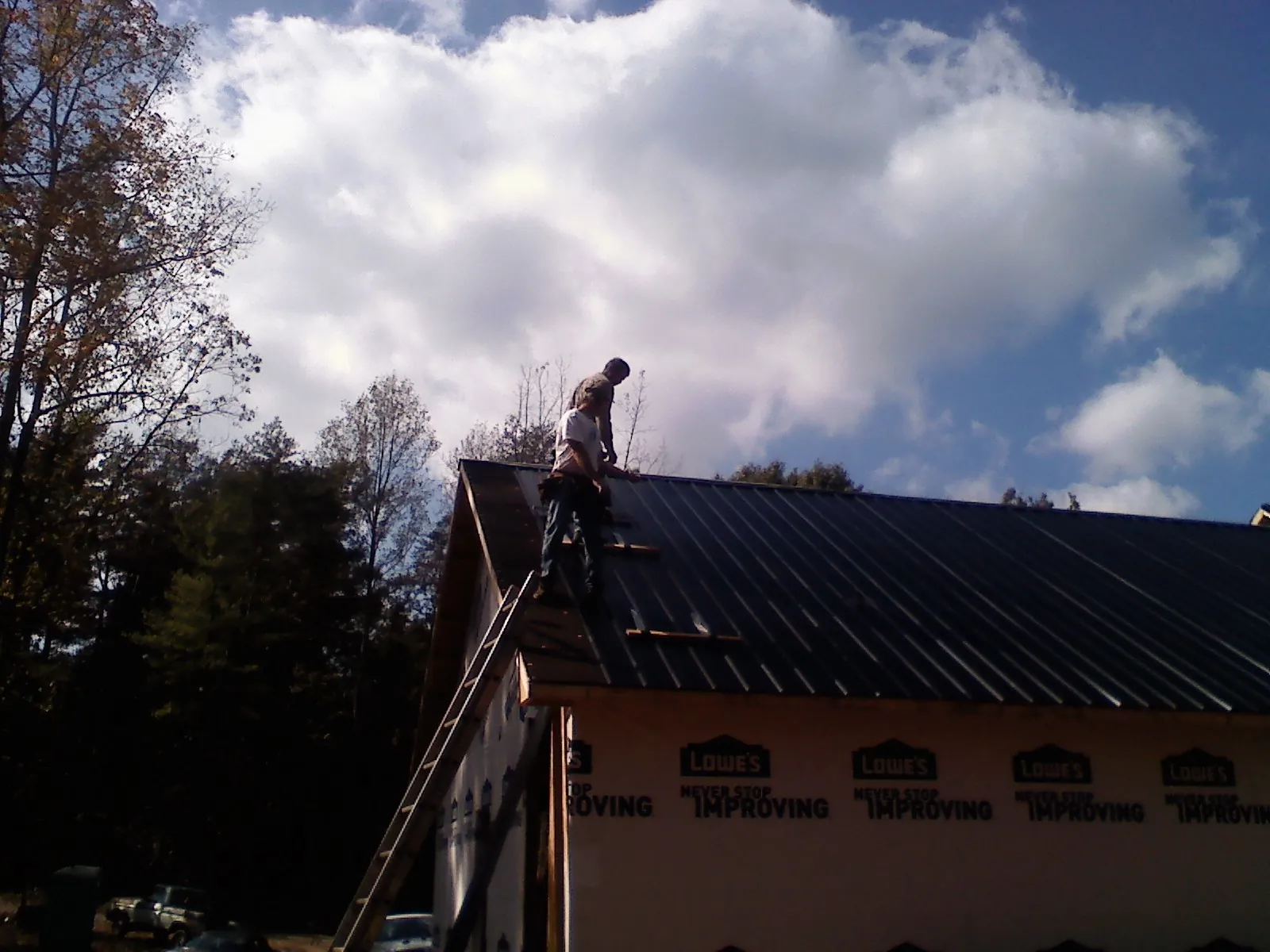 Roofer fastening dark metal panels high against a cloudy sky, from a Roof Inspection job in Middlebury Center