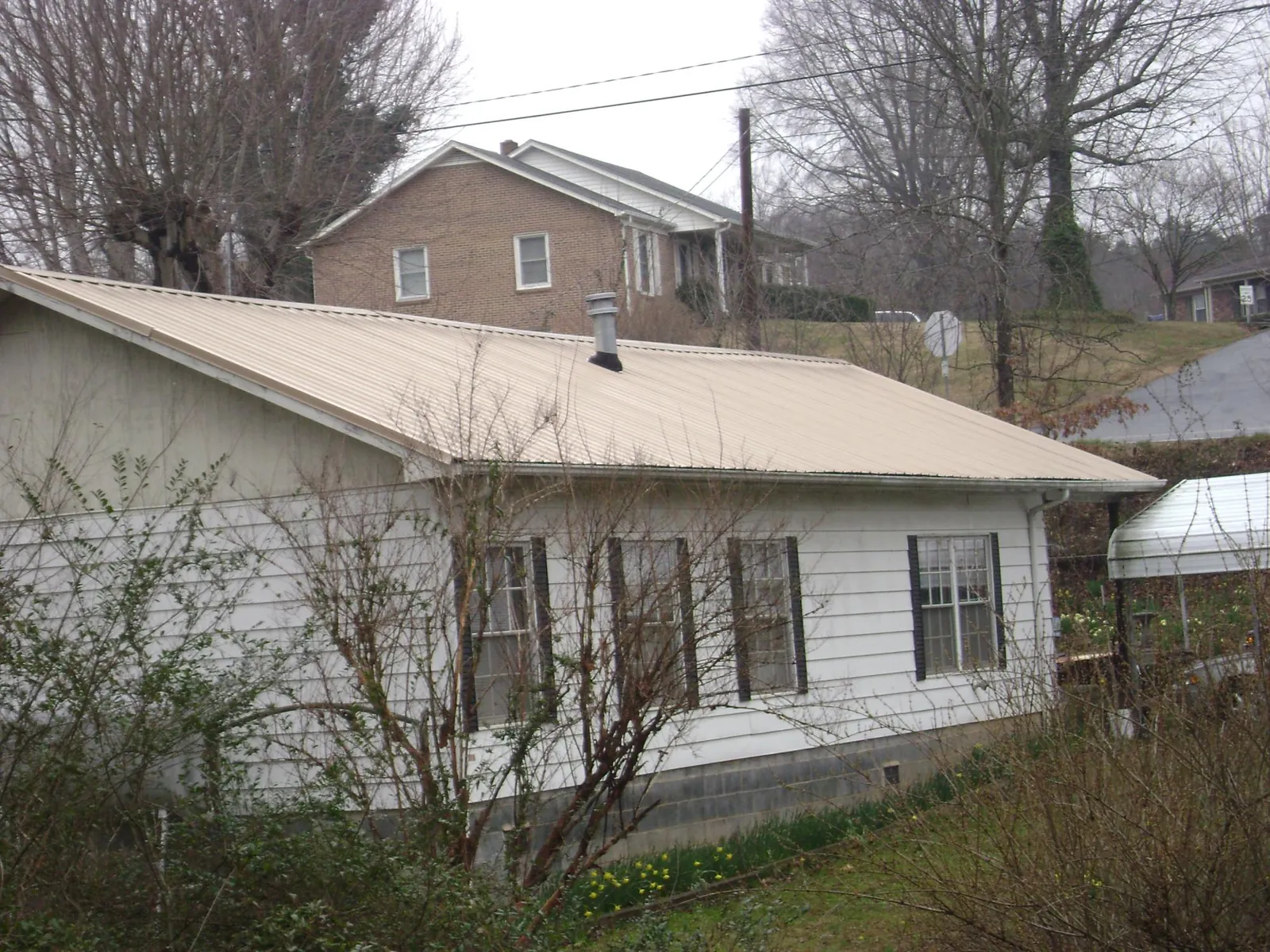 Tan metal roof on a white sided house set into a hillside — Commercial Roofing by Roofing Brothers in Middlebury Center