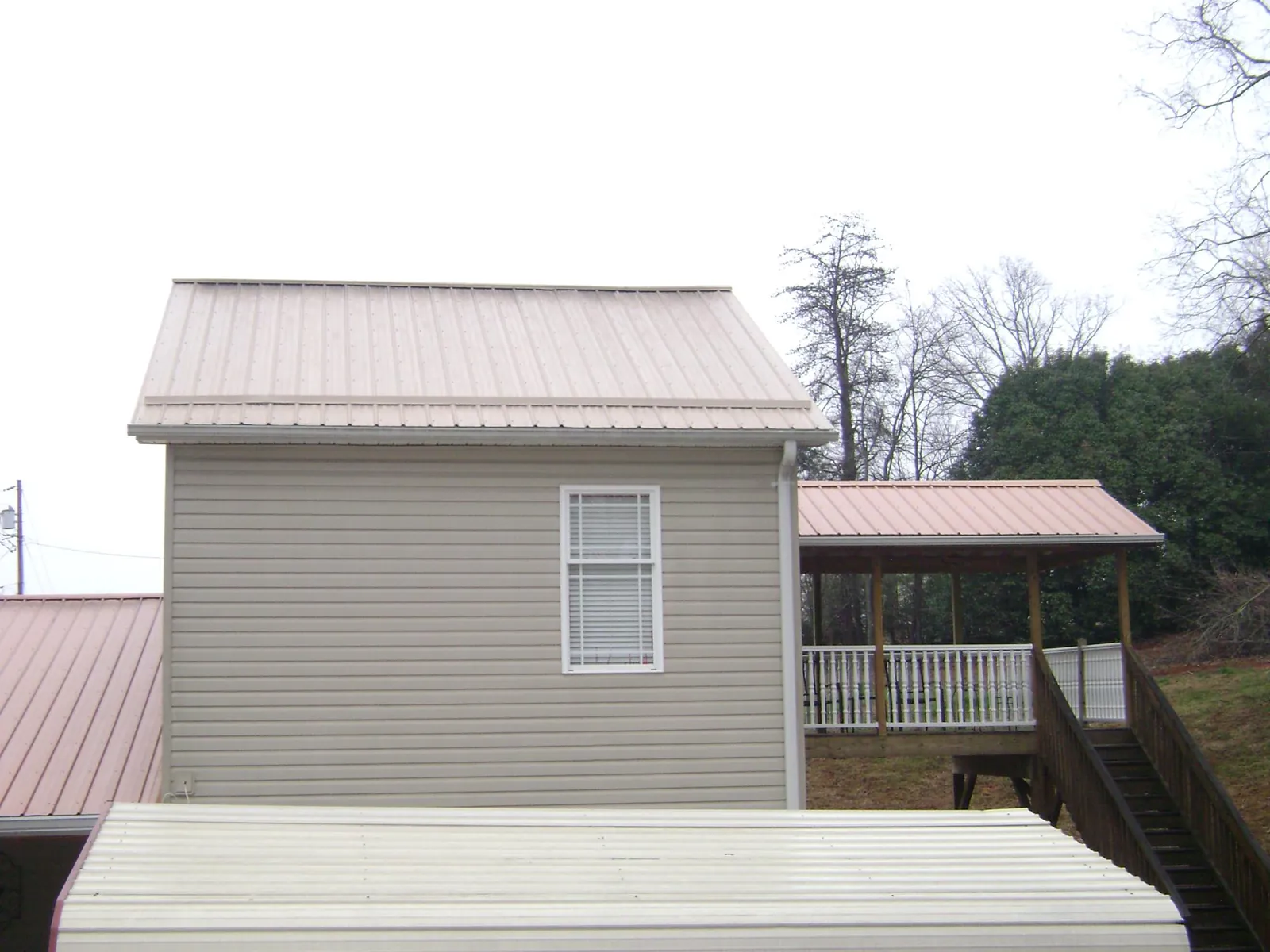 Tan metal roofs on a two story addition and attached porch, from a Roof Replacement job in Middlebury Center